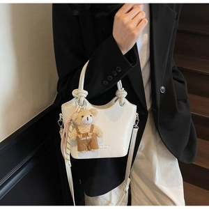 Close-up of white crocodile embossed leather bucket bag with cute bear plush charm