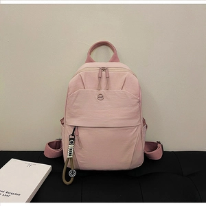 Detail of light pink nylon backpack featuring KMC logo and smiling face pendant charm