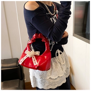 Close-up of red patent leather moon bag with lace bow and pearl heart charm detail