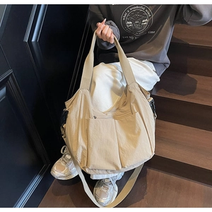 Detail view of a large beige canvas tote bag with front pockets and adjustable strap