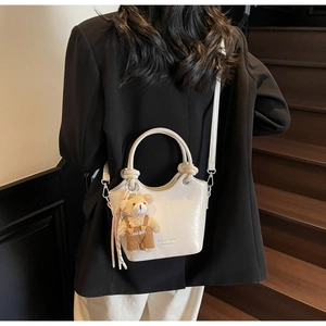 Detail of white crocodile pattern bucket bag with bear pendant on female model
