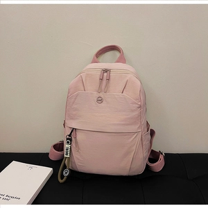 Detailed close-up of light pink water-resistant nylon backpack with NMG metal logo and charm