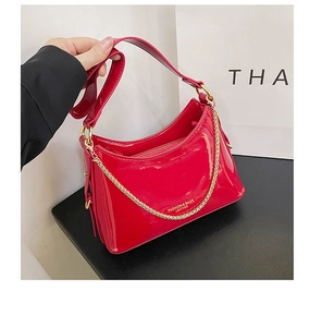 Detail of red glossy patent leather shoulder bag with golden chain and fashion branding