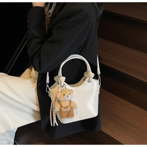 Detail of white crocodile pattern bucket bag featuring a plush bear charm and handle