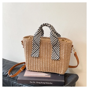 Détail d'un sac cabas en paille avec poignée en tissu rayé et bandoulière en cuir marron