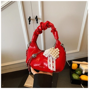Detail of red glossy leather crescent bag with ruched handle and pearl heart pendant