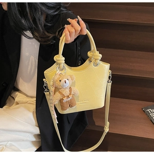 Close-up of yellow crocodile texture bucket bag with cute bear charm and metal hardware