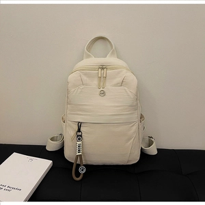 Close-up of beige nylon backpack with NMC metal badge and TREND pendant on leather bench