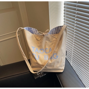 Détail du sac fourre-tout en toile beige minimaliste avec lettrage bleu et doublure à carreaux