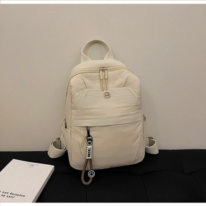 Detail of cream nylon backpack with thickened handle and smile pendant on a bench