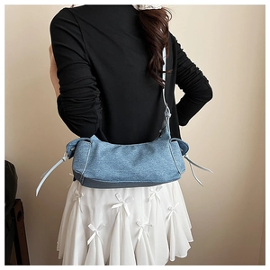 Gros plan d'un sac d'épaule en jean bleu avec des nœuds blancs porté par un mannequin