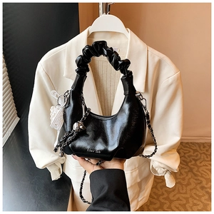 Detail of black pleated handle bag featuring lace bow pendant and removable metal chain