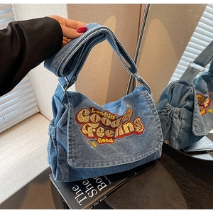Detail of vintage blue denim crossbody bag with white embroidery and adjustable strap