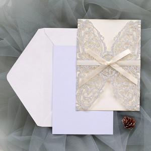 Detailed laser-cut wedding invitation set with silver glitter and a white satin ribbon bow