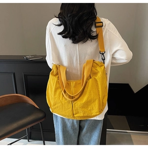 Detail view of large yellow nylon tote bag with wide shoulder strap worn by a model
