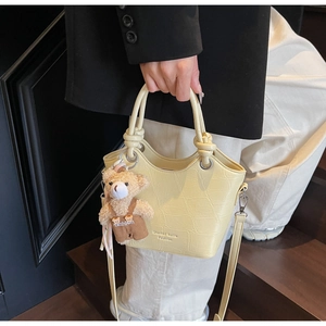 Detail of cream croc-effect bucket bag with knotted handles and a cute bear charm