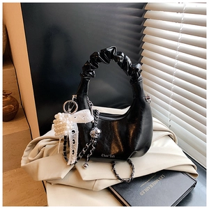 Detailed view of black hobo bag with pleated handle, pearl charms, and lace bow decor