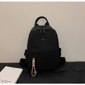 Detail of black nylon backpack featuring dual zippers, logo patch, and trend pendant
