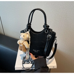 Close-up of black crocodile pattern handbag featuring a cute bear plush keychain detail