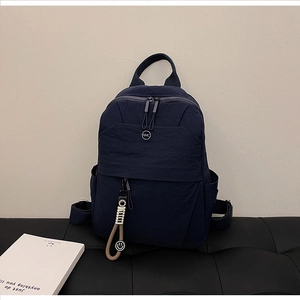 Navy blue nylon backpack with NMC logo and smiley charm on a black leather bench