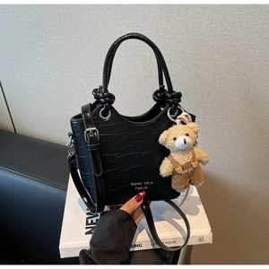 Detailed close-up of a black crocodile-embossed bucket bag with a cute bear charm