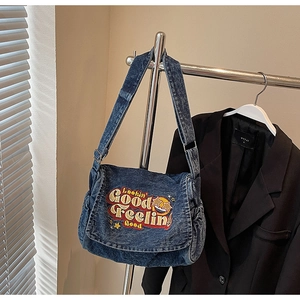 Detail of vintage blue denim bag featuring retro embroidery and adjustable strap