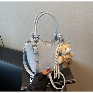 Detail of light blue croc-embossed bucket bag with teddy bear charm and metal eyelet handle