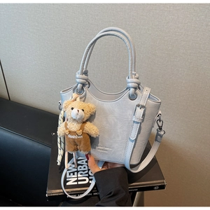 Close-up of light blue crocodile texture handbag with metal rings and bear charm