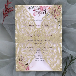 Close-up of laser-cut wedding invitation with gold glitter case and floral inner card