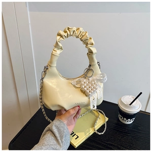 Detail of pleated handle bag with pearl heart charm and lace bow on wooden desk