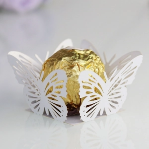 Macro shot of laser-cut white butterfly paper wrap holding a round gold chocolate truffle