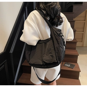 Detailed look at black oversized pleated tote bag with wide strap on shoulder
