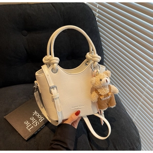 Detail of white crocodile embossed bucket bag with knotted handle and cute bear charm