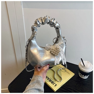 Detailed view of silver metallic pleated handbag with pearl heart bow and chain strap