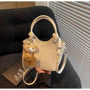 Detail of a creamy white bucket bag with crocodile texture and a brown bear pendant