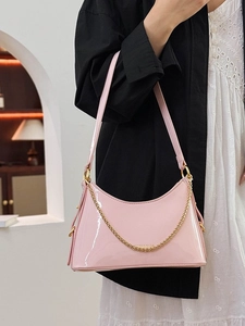 Pink patent leather underarm bag with gold chain strap, shown on model with shoulder carry