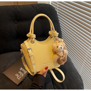 Detail of cream yellow crocodile embossed handbag featuring a knot handle and teddy bear charm
