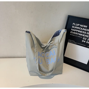 Détail d'un sac cabas en nylon gris avec doublure à carreaux bleus et décor nœud
