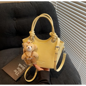 Detail of yellow crocodile pattern handbag with plush bear charm on a velvet chair