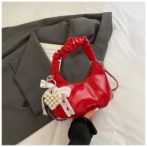 Detail of red pleated hobo bag featuring lace bow, pearl charm, and gold chain strap