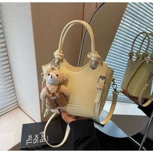 Close-up of yellow crocodile texture leather bucket bag with cute teddy bear charm