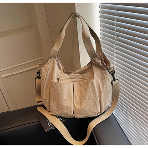 Detail of a beige nylon tote bag featuring front pockets and adjustable shoulder strap