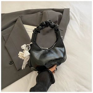 Detail of black glossy pleated handbag with pearl lace charm and silver zipper accent