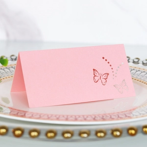 Detail of pink laser-cut butterfly place card on a white dinner plate for wedding