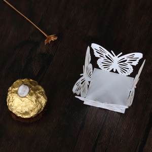 Detail of white laser-cut butterfly cupcake wrapper on a dark wood background