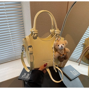 Close-up of yellow crocodile texture bucket bag with a cute bear plush keychain detail