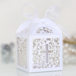 Detail of white laser-cut favor box with hollow cross design and white silk ribbon bow