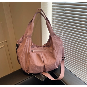 Close-up of a pink nylon tote bag with multiple front pockets on a leather bench
