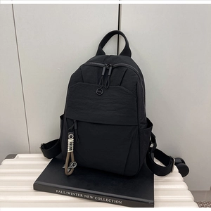 Detail of black nylon backpack featuring bead charms and NMC logo on a suitcase