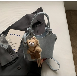 Detail of light blue faux crocodile bucket bag with cute plush bear charm on grey fabric